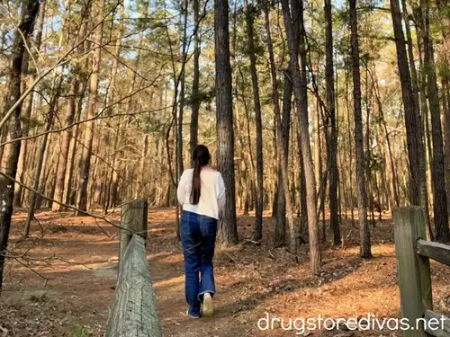 A woman in a white shirt and jeans hiking on a trail through trees at Santee State Park in Santee, SC.