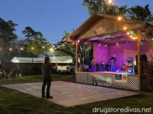 A wooden pavilion with a band on it with a dance floor in front with a man on it, all at nighttime.