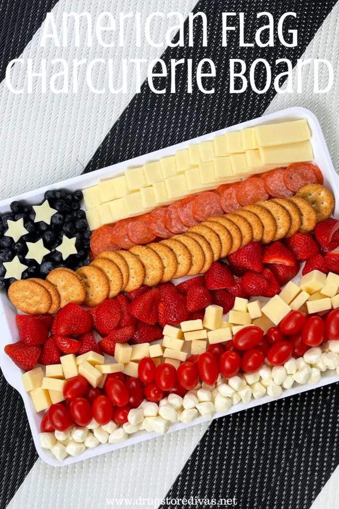 A rectangular tray filled with cheese, fruit, and crackers arranged to look like an American flag with the words "American Flag Charcuterie Board" digitally written on top.