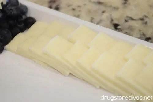 Blueberries in a corner and slices of white cheese in two rows on a white tray.