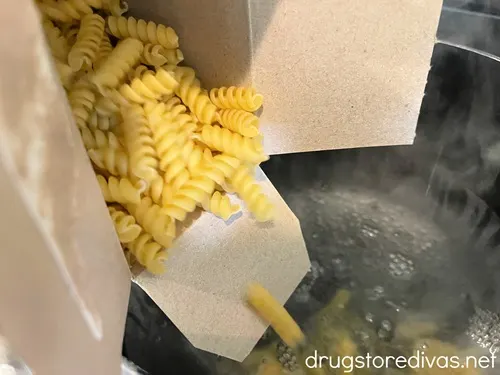 Rotini pasta being poured from a box into boiling water.