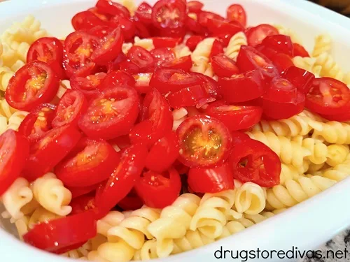 Sliced grape tomatoes and cooked rotini pasta in a white bowl.