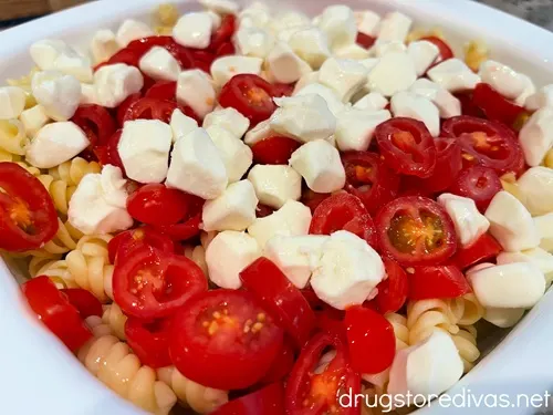 Mozzarella pearls, sliced grape tomatoes, and cooked rotini pasta in a white bowl.