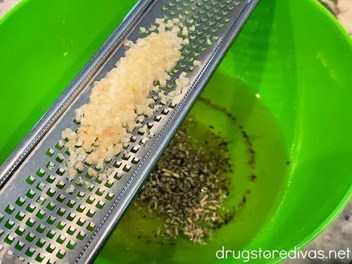 Grated garlic on a grater above a green bowl filled with oil and seasoning.