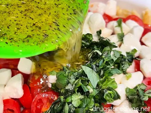 Dressing in a green bowl being poured over caprese pasta salad.