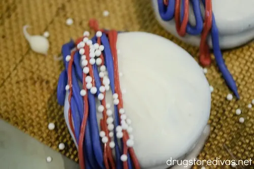 White Oreo cookies with blue and red lines and white nonpareil sprinkles on one half.