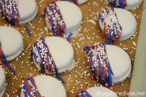Nine white Oreo cookies with blue and white lines and white nonpareil sprinkles on them on a baking sheet.