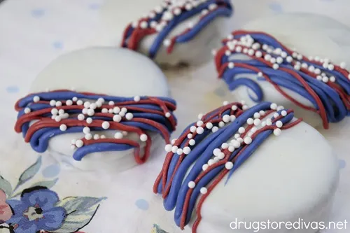 Four white Oreo cookies with blue and white lines and white nonpareil sprinkles on them on a white napkin.
