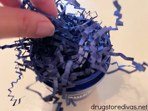 Two fingers putting Blue paper shred into a blue mini paint bucket.