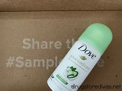 A Dove body spray canister with a green cap on top of a brown box with the words share the sample behind it.