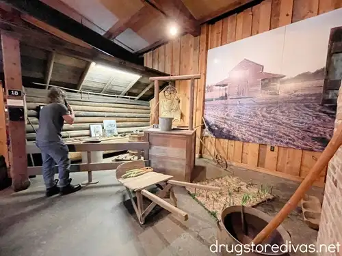 A man listening to a handset in the Elloree History Museum around a display with a wooden well, plow, and other period pieces.