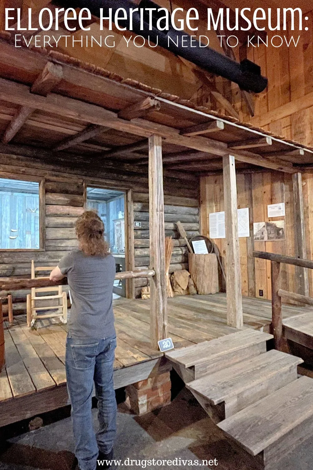 A man in a gray shirt and jeans looking at a wooden cabin in a museum with the words 
