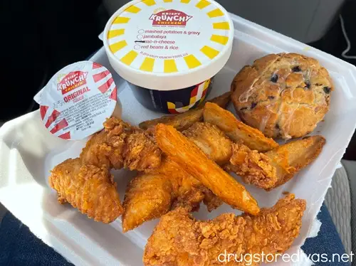 Chicken fingers, a biscuit, and fries, plus a container of food and a container of sauce, in a styrofoam to go container from Krispy Krunchy Chicken.