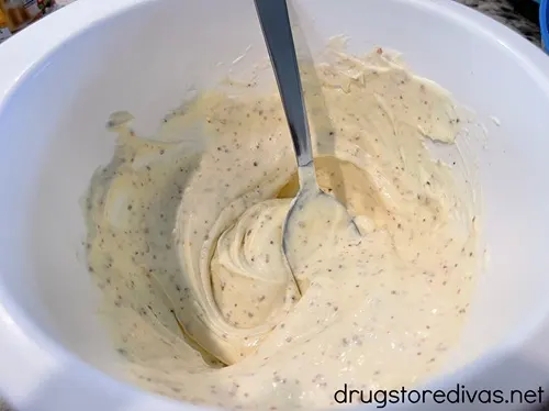 A mayonnaise based dressing with a spoon in it in a white bowl.