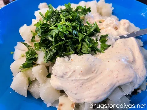 Cilantro and a mayonnaise dressing on top of cooked potato cubes in a blue bowl.