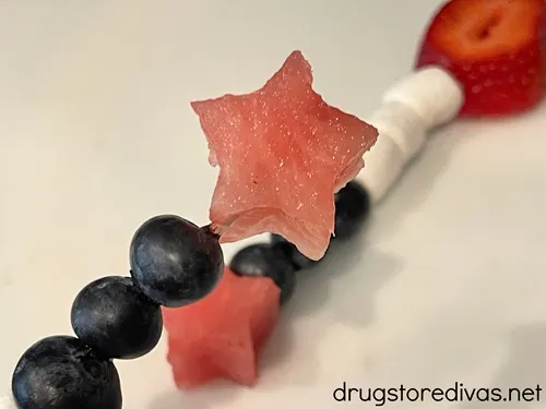 A star-shaped piece of watermelon and three blueberries on a skewer with a fruit skewer behind it.