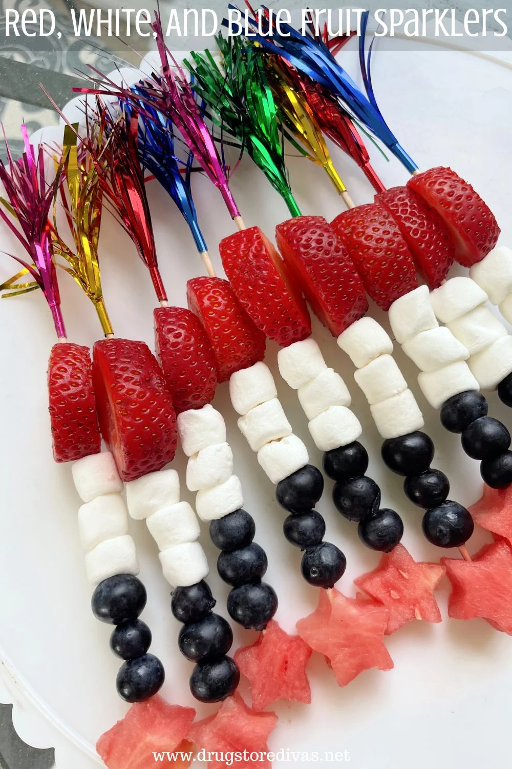 Skewers with colored foil on one side, filled with a slice of strawberry, three mini marshmallows, three blueberries, and a watermelon star at the end with the words 
