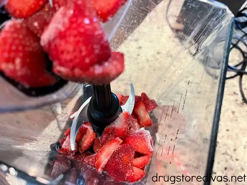 Frozen strawberry halves being added to a blender.