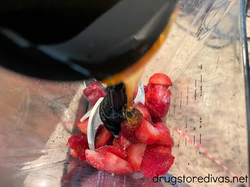 Honey in a black measuring cup being added to a blender that has strawberries in it.