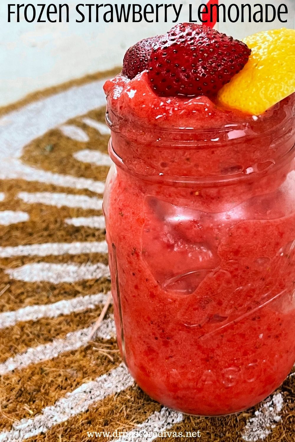 A mason jar filled with a red frozen drink with strawberries and lemon on top and the words 