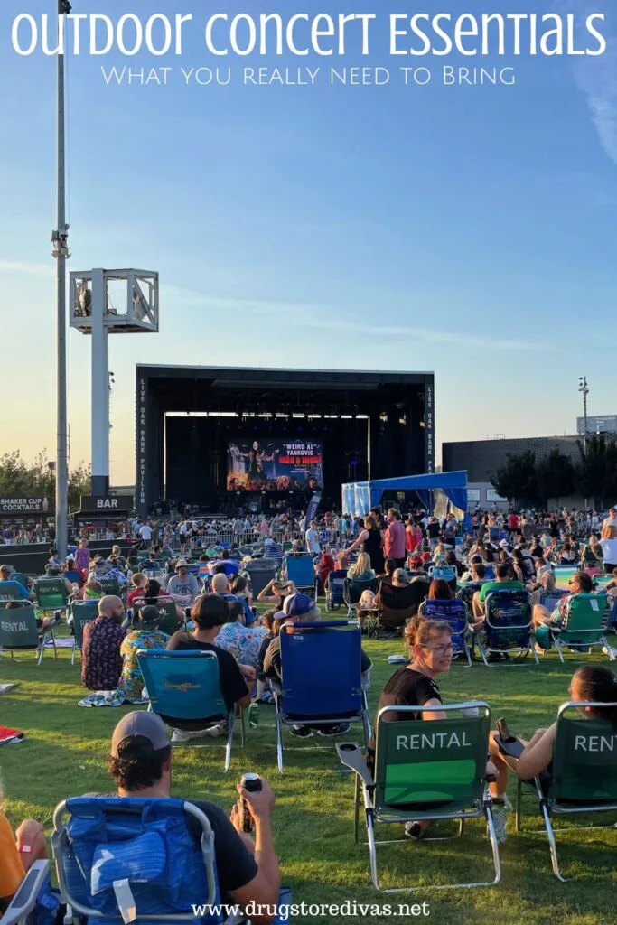 An outdoor concert, from the perspective of the lawn seats, with the words "Outdoor Concert Essentials: What You Need To Bring" digitally written on top.