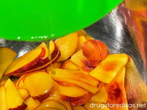 A vinaigrette in a green bowl being poured over peach slices that are in a silver bowl.