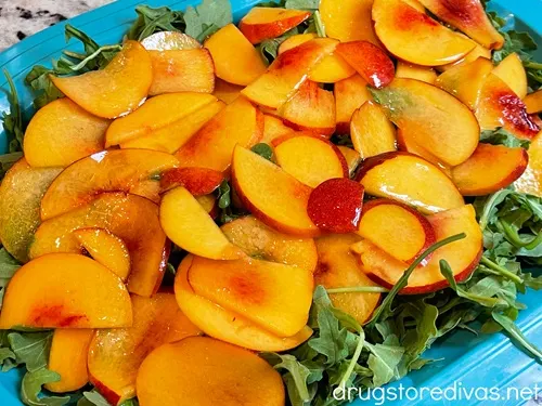 Peach slices on top of arugula in a blue tray.