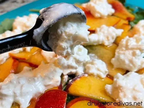 A measuring spoon with burrata filling in it over peach slices and burrata filling.