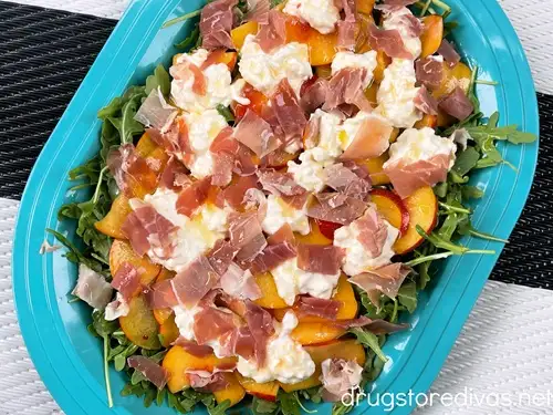 Peach and arugula salad with burrata and prosciutto on a blue tray.