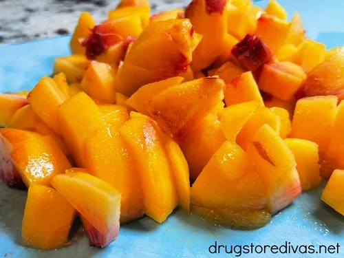 Peeled and diced peaches on a blue cutting board.