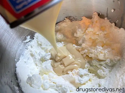Sweetened condensed milk being poured from a can into a bowl with whipped cream.
