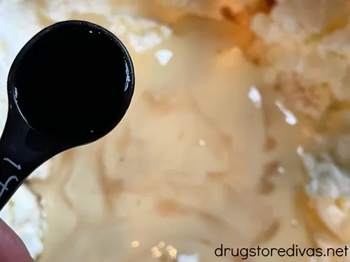 A measuring spoon of liquid over a bowl filled with a white-ish liquid.