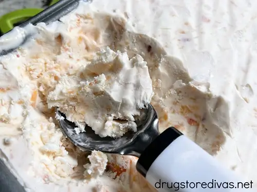 A bread pan filled with peach ice cream and some scoops removed with an ice scooper.