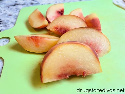 Peach slices on a green cutting board.