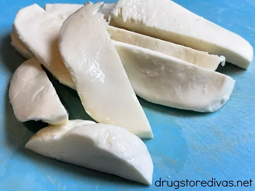 Mozzarella cheese slices on a blue cutting board.