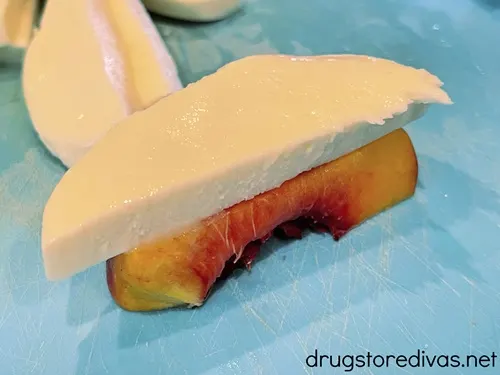 A piece of mozzarella cheese on top of a piece of peach.