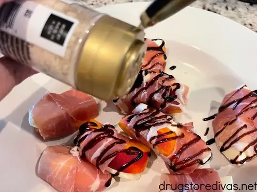 Salt in a bottle being drizzled on top of a tray of prosciutto wrapped peach and mozzarella slices.