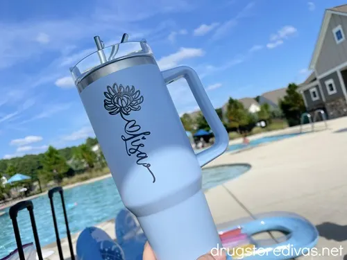 A blue tumbler with a handle that says "Lisa" on it in front of a pool.