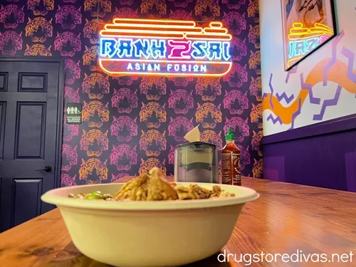 A bowl of food on a table with a neon sign on the wall behind it that says "Bahn Sai Asian Fusion" in The Cargo District in Wilmington, NC.