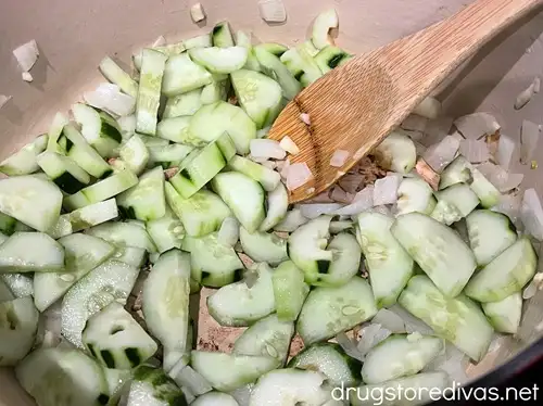Chopped onion, garlic, and sliced cucumbers in a Dutch oven with a spoon.