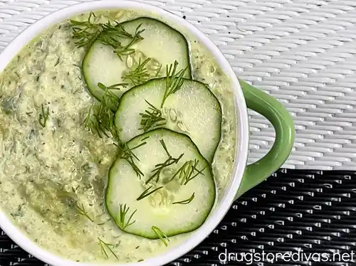 Cucumber soup in a green bowl with a white rim with slices of cucumber and dill on top as a garnish.