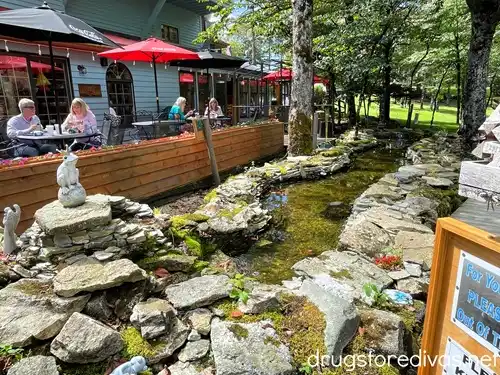Patio tables with umbrellas with diners at them between a building and a manmade rock pond at Fred's General Mercantile in Beech Mountain, NC.