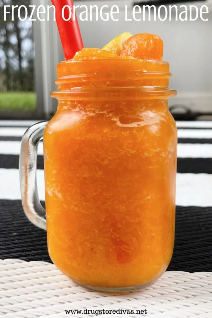 A mason jar with a handle filled with an orange frozen drink and a red straw on a black and white mat with the words "Frozen Orange Lemonade" digitally written on top.