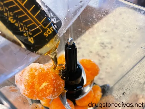Honey in a measuring cup being poured over mandarin oranges in a blender.