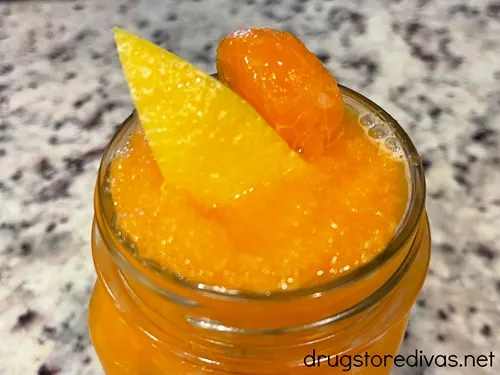 A glass of frozen orange lemonade with a piece of mandarin orange and lemon in it.