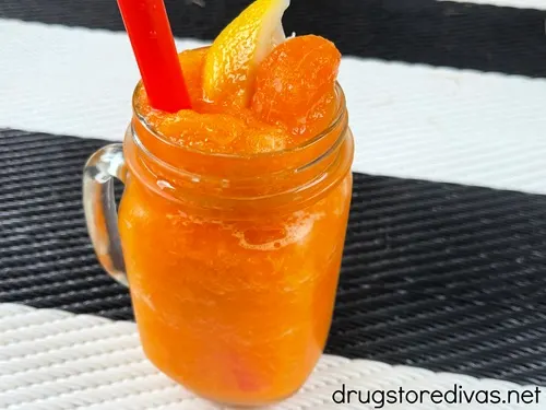 A glass of frozen orange lemonade with a piece of mandarin orange and lemon and a red straw in it on a black and white rug.