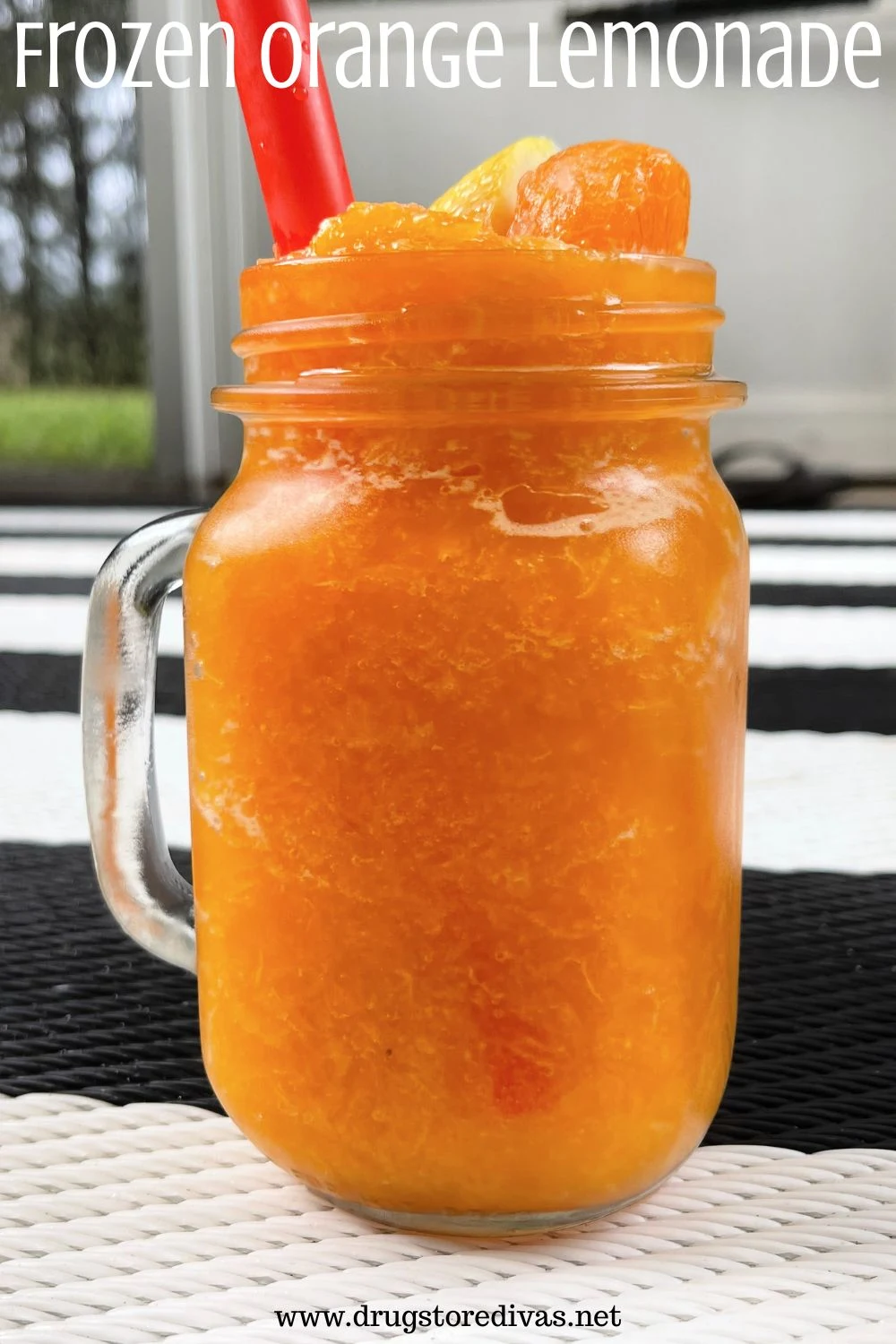 A mason jar with a handle filled with an orange frozen drink and a red straw on a black and white mat with the words 