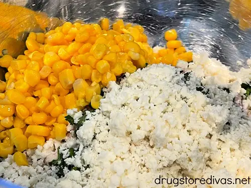 Corn and cotija cheese and chopped chicken in a silver bowl.