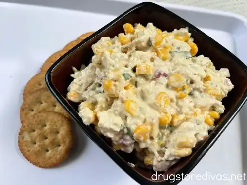 Mexican street corn chicken salad in a black bowl with crackers next to it.