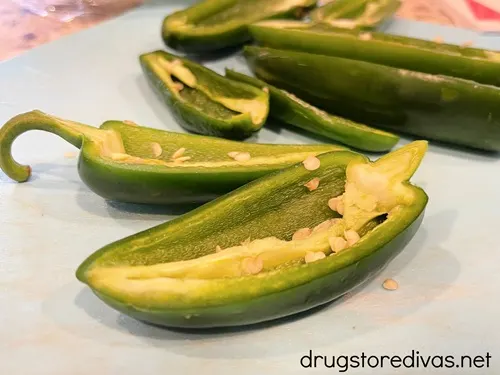 Jalapeno pepper halves on a blue cutting board.